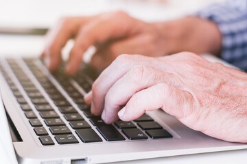 Older person's hands typing on a gray laptop.