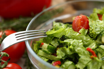 Focused photo on glass bowl being filled of fresh salad, time to have dinner
