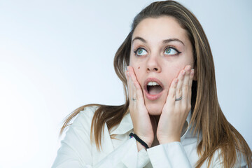 ragazza bionda con camicia bianca si porta le mani alla faccia e guarda lontano con aria meravigliata, isolata su sfondo chiaro