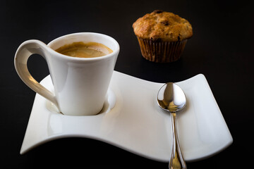 Espresso coffee in a wave shaped cup and saucer on black background with chocolate chip muffin on the side.