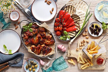Chicken wings, roasted vegetables, grilled tortilla and appetizers variety serving on party outdoor table. Mediterranean dinner table concept. Overhead view.