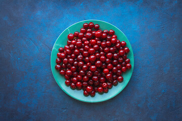 Round green plate with fresh red delicious cherries on blue background. Top view
