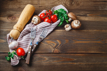 Tomatoes, garlic, champignons, parsley, pepper shaker, forks and napkin on wooden background