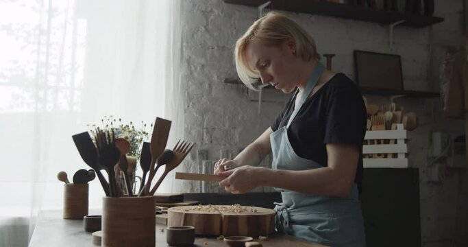 Woman carpenter carves piece of wood making a spoon