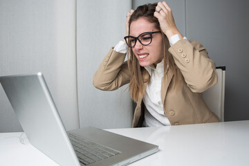 ragazza biondacon occhiali da vista ,  vestita con una giacca beige è seduta nella sua postazione di lavoro di fronte al portale, si arrabbia e scuote urla disperata