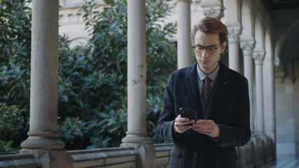 Student receiving good news on phone. Businessman walking in colonnade hallway