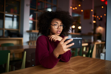 Young female sitting in coworking space with modern smartphone