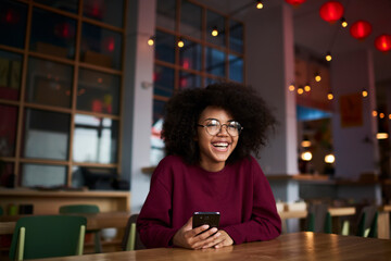 Charming smiling teen girl having fun during free time in cafe indoors chatting with friend