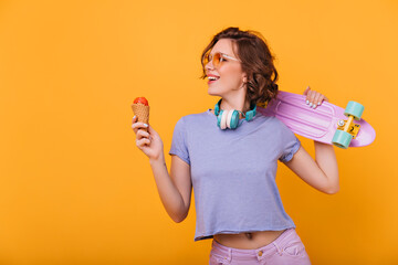Slim european lady with tasty ice cream smiling on bright background. Enthusiastic female model with skateboard enjoying favorite dessert. © Look!