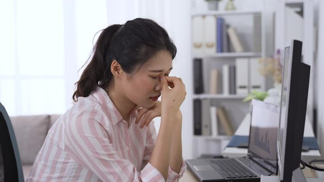 asian female supervisor troubled with eye fatigue let out a sigh. taiwanese lady propping head is having dry eyes while looking at data on computer. health and eye care concept