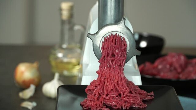 Preparation of minced fresh beef through electric meat grinder on background with onion, garlic and olive oil. Meat cooking concept. Food background