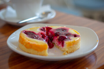 Cut cheesecake with a cherry on a white plate on a wooden table.
