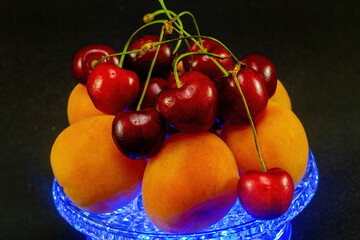 Still life with apricot and cherry with blue illumination on a black background.