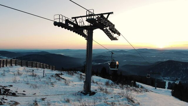 cabins of modern poma lift over high mountain snowy steepy slope with pine trees at famous ski resort in early morning aerial view
