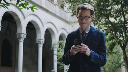 Fototapeta premium Student using smartphone on university territory. Man typing on phone phone