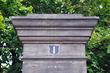 Close Up of Carved Stone Gatepost with Number One in Painted Shield with Woodland Background 
