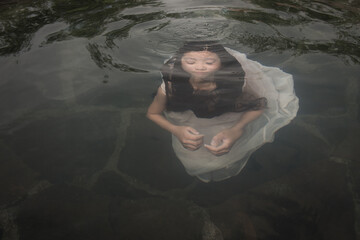 Girl in white dress swimming under water towards surface