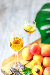 Apricot liqueur in shot glass and fresh apricots on a light wooden table.