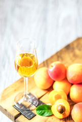 Apricot liqueur in shot glass and fresh apricots on a light wooden table.