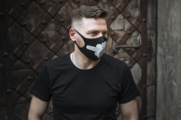 Stylish brutal guy in a fashionable black protective face mask with a white pattern. A man with a stylish haircut on the street, looking to the side.