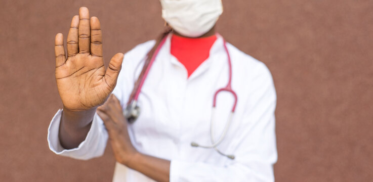 coronavirus stop concept. African American girl doctor, in a protective mask, white coat, shows her hand to stop the coronavirus infection, covid 19-20.