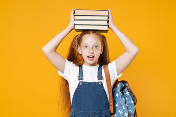 Young fun redhead girl 12-13 years old in white t-shirt backpack hold on head big stack school textbook notebook books isolated on yellow background children studio portrait Kids education concept - obrazy, fototapety, plakaty