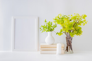 Home interior with decor elements. White frame, branches with green leaves in a vase, interior decoration