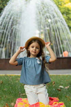 Image of a little girl in a straw hat on the background of a fountain in a hat