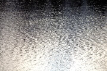 Silver surface of wavy water with bright highlights and reflections. Ripples on water surface close-up. Glowing surface of the water. Silver metal surface with highlights close-up. Abstract background