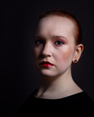Portrait of a young woman, dressed in black and wearing heavy make up.