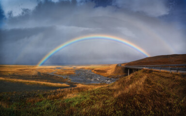 Panorama view of icelandic nature landscape. Rainbow after rain, road and river. West Iceland region