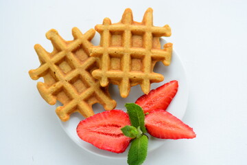 Belgian waffles with strawberry and mint on white plate on light background
