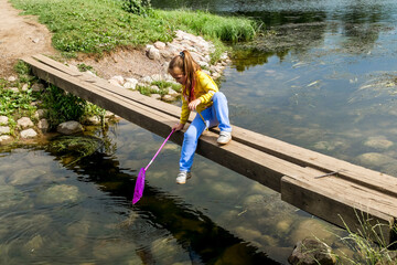 Fototapeta na wymiar A girl with a net sits on a bridge across a river on a summer day