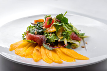 Mix - mango salad, with jerky, grapefruit, pine nuts and mint, on a white plate, white background