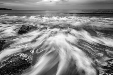 Stunning black and white long exposure seascape with rocks and motion blur waves.