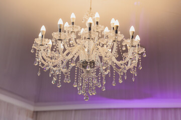 small lamp as stars at big chandelier with many crystals.