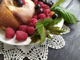 Pie with berries red ripe raspberries black currant green leaves on a white plate on a lace napkin on a black background