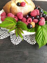Pie with berries red ripe raspberries black currant green leaves on a white plate on a lace napkin on a black background