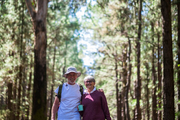 Senior couple enjoy together outdoor leisure activity walking in the forest - beautiful aged people smile and hug with environmental trees background