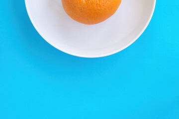 Half part view of orange grapefruit on white plate on blue background. Diet concept, copy space for text