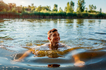Young handsome man swimming in river. Happy guy smiling in water. Summer vacation