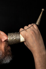 Man with beard drinks from horn on black background