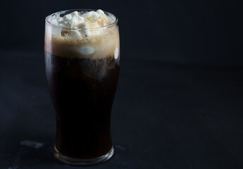 A glass of iced craft beer stout with vanilla ice cream. Refreshing summer cocktail on a dark table
