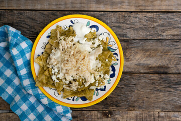 Mexican green chilaquiles with chicken and cheese on wooden background