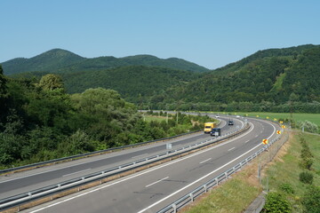 A highway in Slovakia leading among mountainous country. The highway is surrounded on both sides by green vegetation.