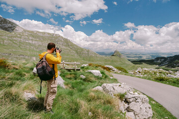 Fototapeta premium travel photographer in mountains. Professional photographer travel in countryside with camera and taking photos. tourist male with backpack on summer vacations. Montenegro, Durmitor. 