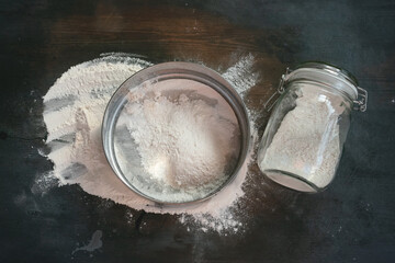Flour, sieve and glass jar on the wooden kitchen table background top view.