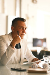 A businessman of 30-35 years old in a white jacket signs important documents.