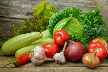 Still life of fresh vegetables with cabbage, zucchini, tomatoes, onions and greens on an old wooden background