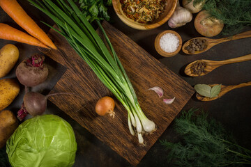 Fresh vegetables for vegetable soup, for borsch (beetroot soup). Cabbage, carrots, beets, onions, potatoes and spices on a cutting wooden board and dark background.